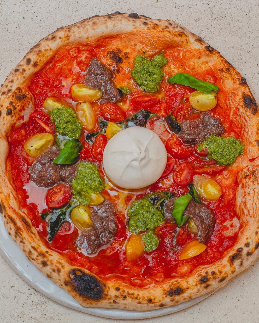 Pizza artesanal napolitana con salsa de tomate, tomates cherry, pesto, hojas de albahaca fresca y una bola de queso burrata en el centro - Pizzería Rifugio Madrid.